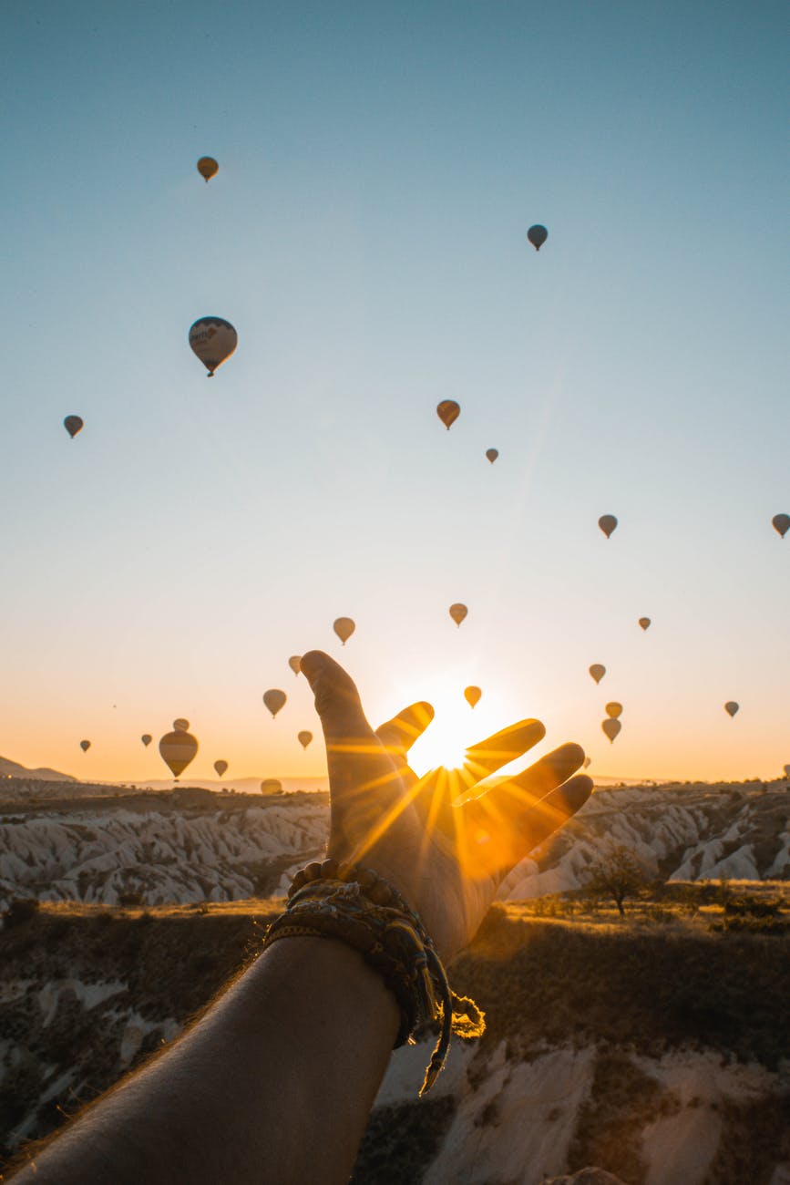 photo of person s hand across flying hot air balloons during golden hour